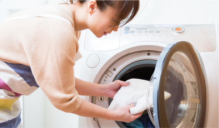 女性が洗濯機に洗濯物を入れる写真